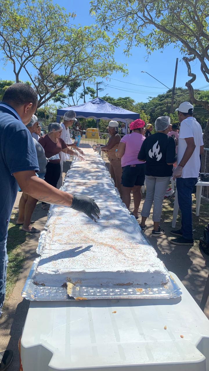 Em meio a Praça na avenida dos Metalúrgicos, sob uma tenda e sobre mesas plásticas brancas enfileiradas está o bolo de 42 metros.  Nas laterais os cozinheiros enfeitam o bolo com cobertura e confetes.